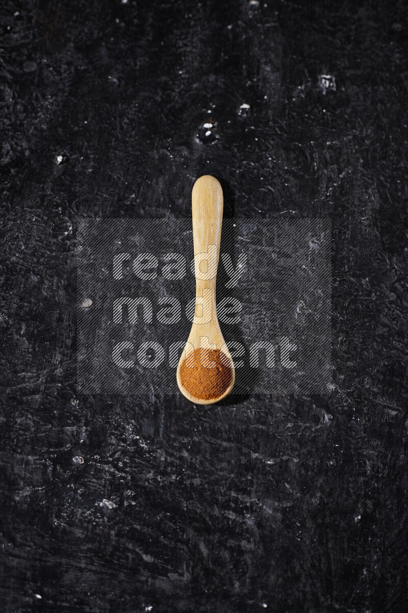 A wooden spoon full of ground paprika powder on black background