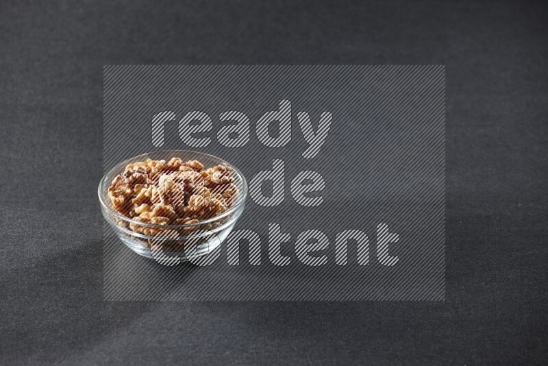 A glass bowl full of peeled walnuts on a black background in different angles
