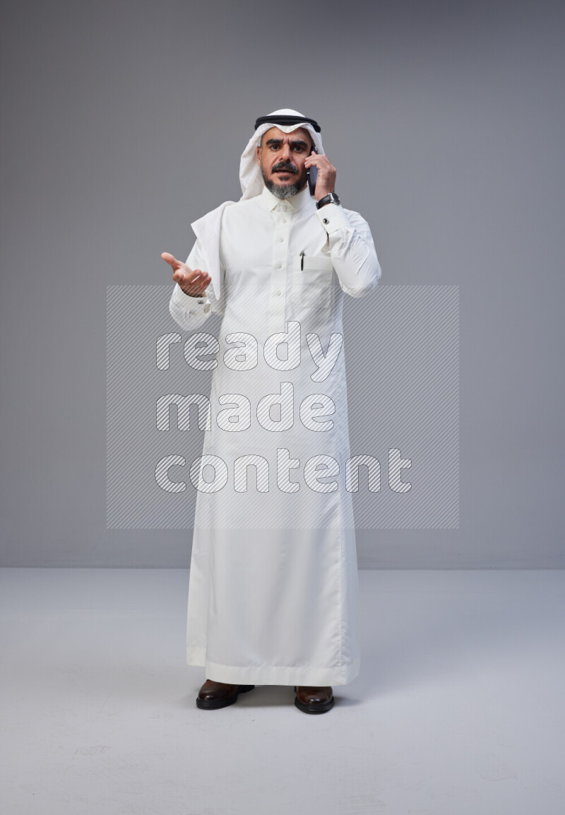 Saudi man Wearing Thob and white Shomag standing talking on phone on Gray background