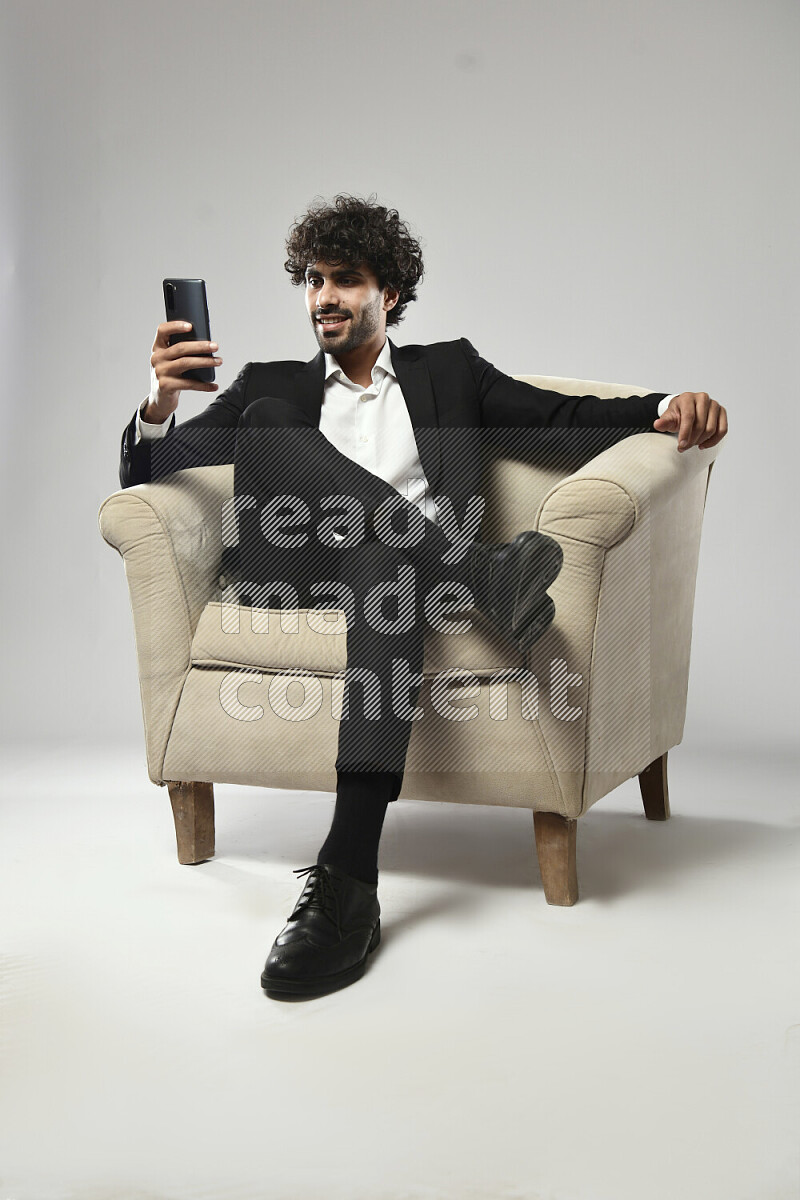 A man wearing formal sitting on a chair texting on the phone on white background