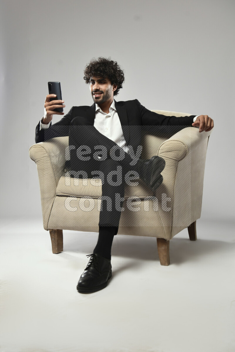 A man wearing formal sitting on a chair texting on the phone on white background