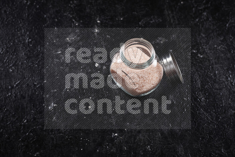 A glass jar full of fine himalayan salt on black background