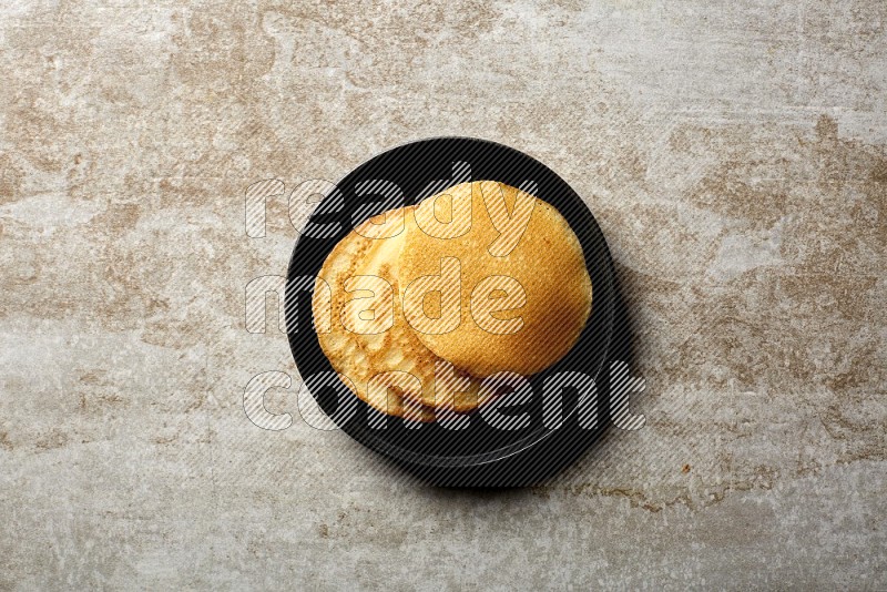 Three stacked plain pancakes in a black plate on beige background