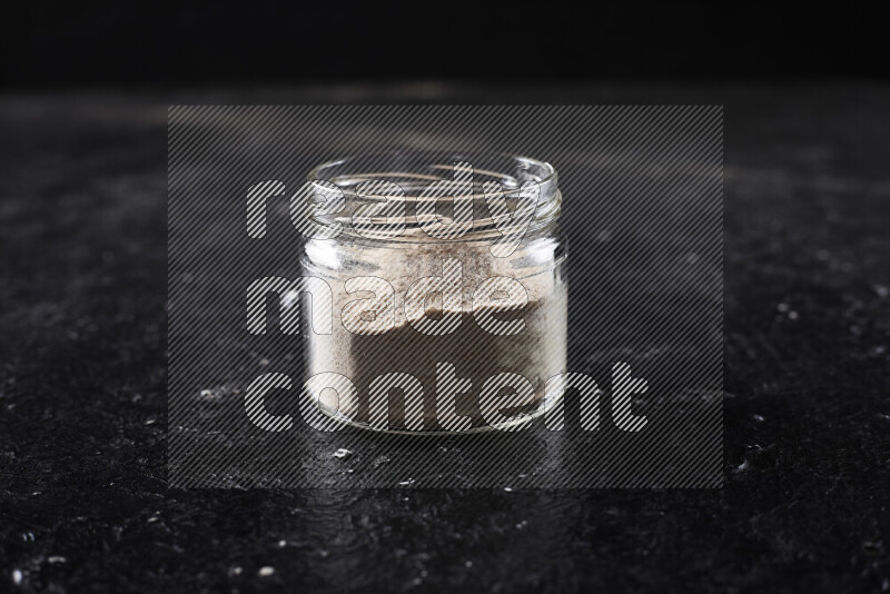 A glass jar full of onion powder on black background