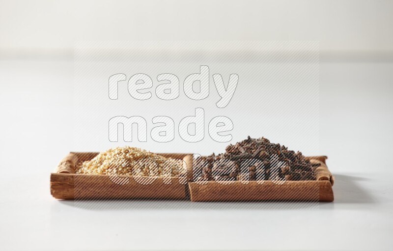 مربعان من أعواد القرفة ممتلئان بالقرنفل وبذور السمسم علي خلفية بيضاء