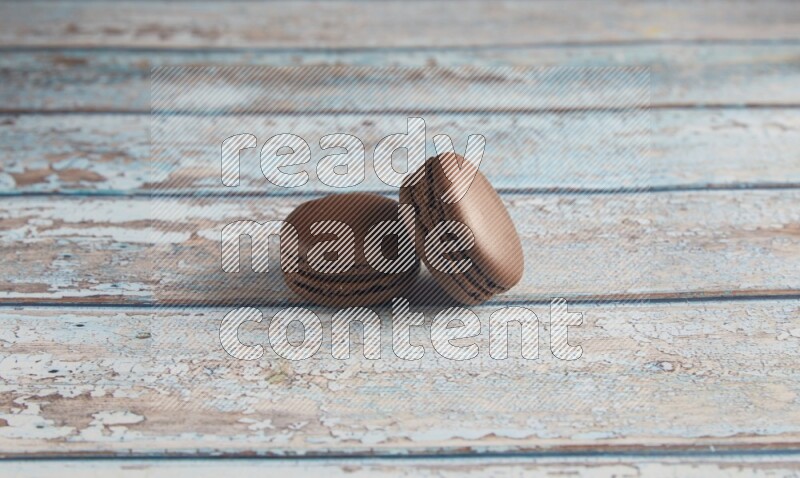 45º Shot of two Brown Dark Chocolate macarons on light blue wooden background