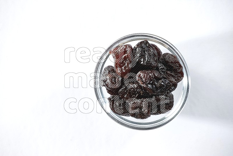 A glass bowl full of dried plums on a white background in different angles