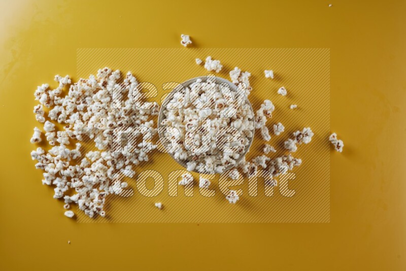 A white pottery bowl full of popcorn with popcorn beside it on a yellow background in different angles