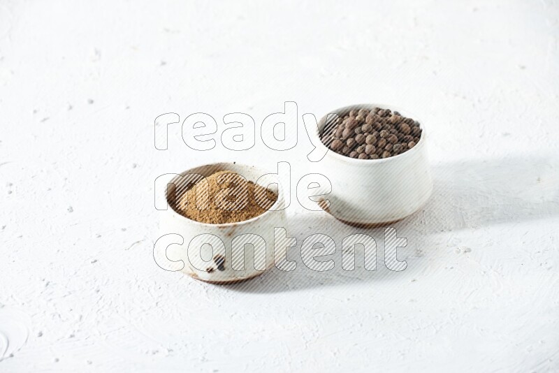 2 beige bowls, one full of allspice powder and the other full of whole balls on a textured white flooring