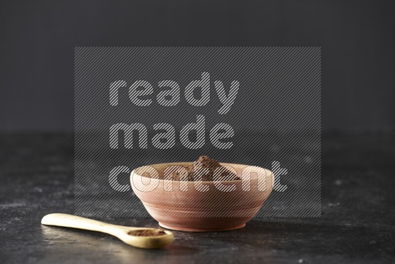 وعاء خشبي وملعقة خشبية ممتلئان ببودرة القرنفل على خلفية سوداء