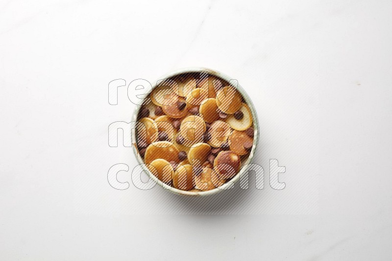 Top-view shot of chocolate chips cereal pancakes in a round bowl on white background