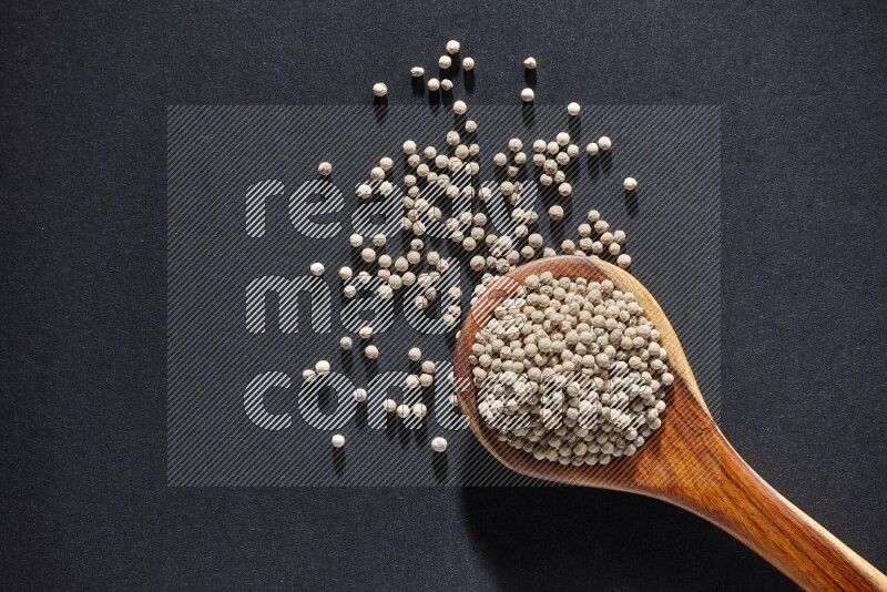 A wooden ladle full of white pepper beads on black flooring
