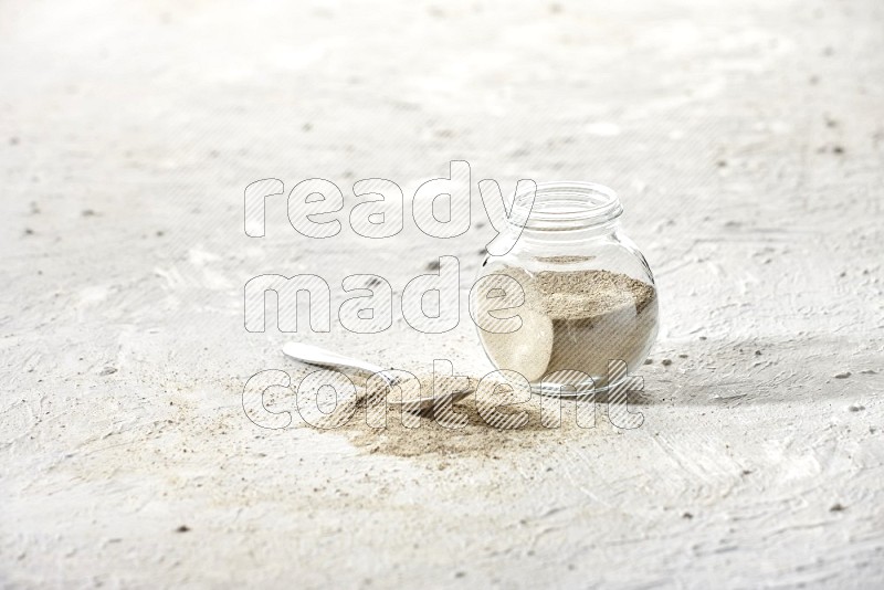 Herbal Glass jar full of white pepper powder and metal spoon full of powder on textured white flooring
