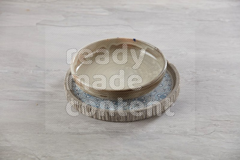 multi color pottery round dish on top of multi color round ceramic plate, on grey textured countertop