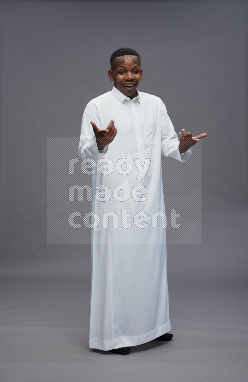 Saudi man wearing thob standing interacting with the camera on gray background