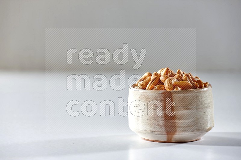 A beige ceramic bowl full of cashews on a white background in different angles