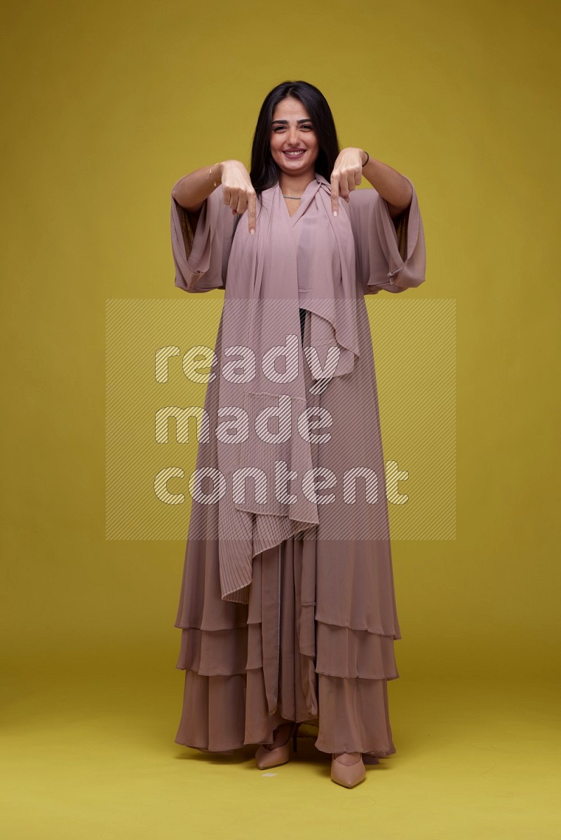 A woman Pointing on a Yellow Background wearing Brown Abaya