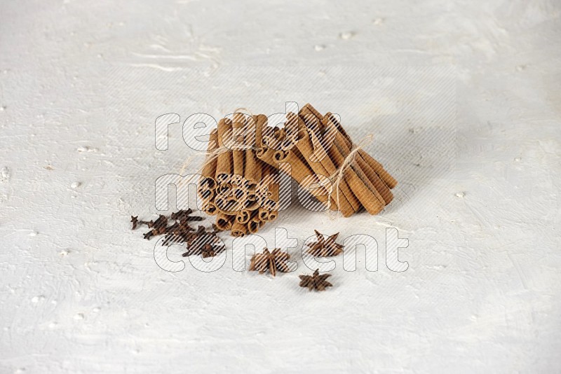 Two bounded stacks of cinnamon sticks with cloves and star anise on white background