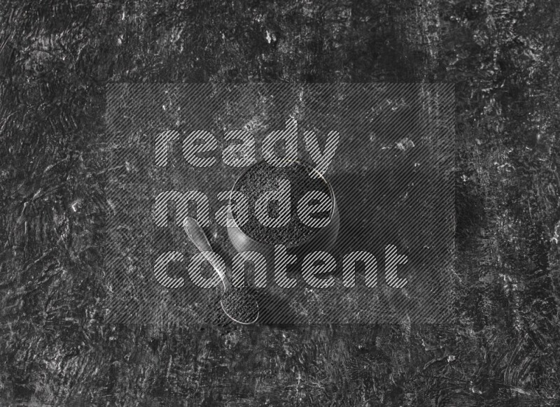 وعاء فخاري أسود وملعقة معدنية ممتلئان ببذور حبة البركة علي خلفية سوداء