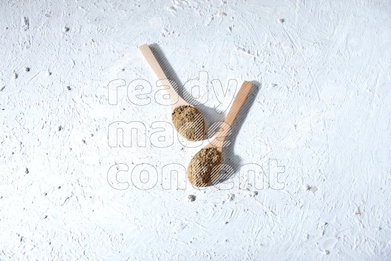 ملاعق خشبية ممتلئة ببودرة بهار الفلفل الحلو مع الحبوب متناثرة على خلفية بيضاء