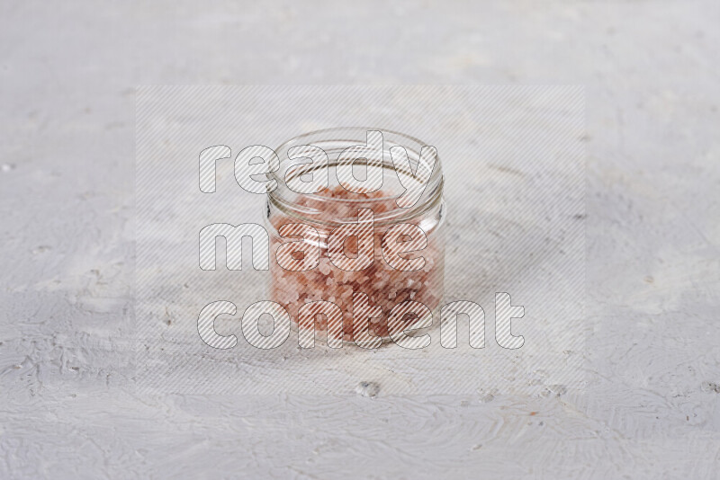 A glass jar full of coarse himalayan salt crystals on white background