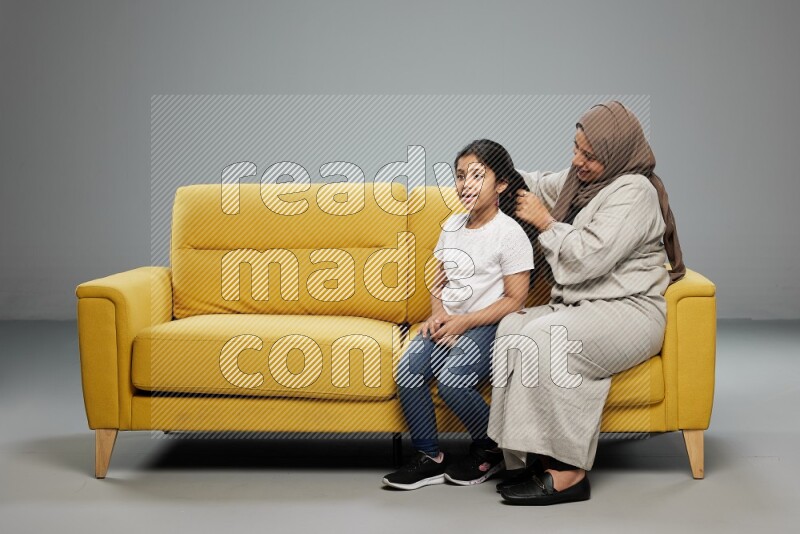 A mother sitting styling hair for her daughter on gray background