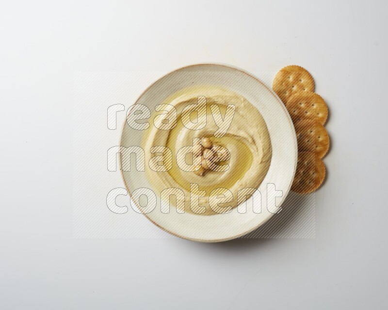 Hummus in a pottry plate garnished with roasted chickpeas on a white background