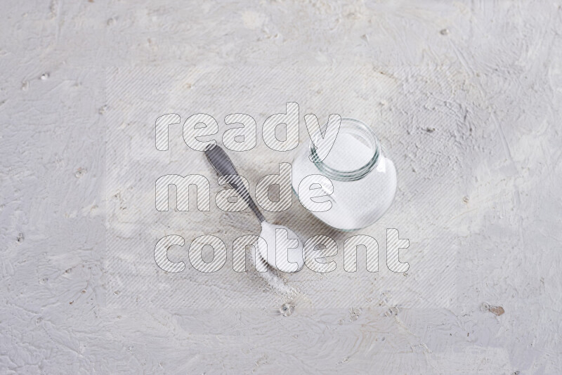 A glass jar full of fine table salt on white background