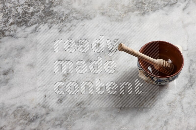 Decorative pottery pot with wooden honey dipper in it on grey marble background