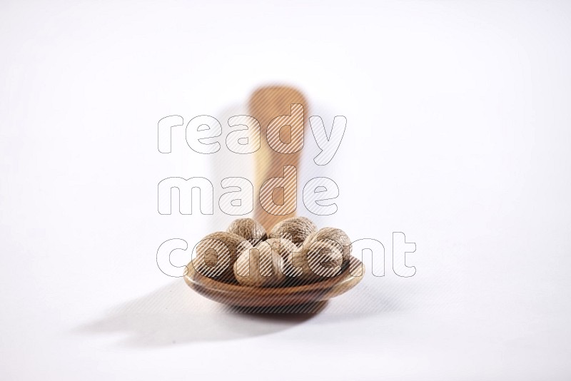 A wooden ladle full of whole nutmeg seeds on a white flooring