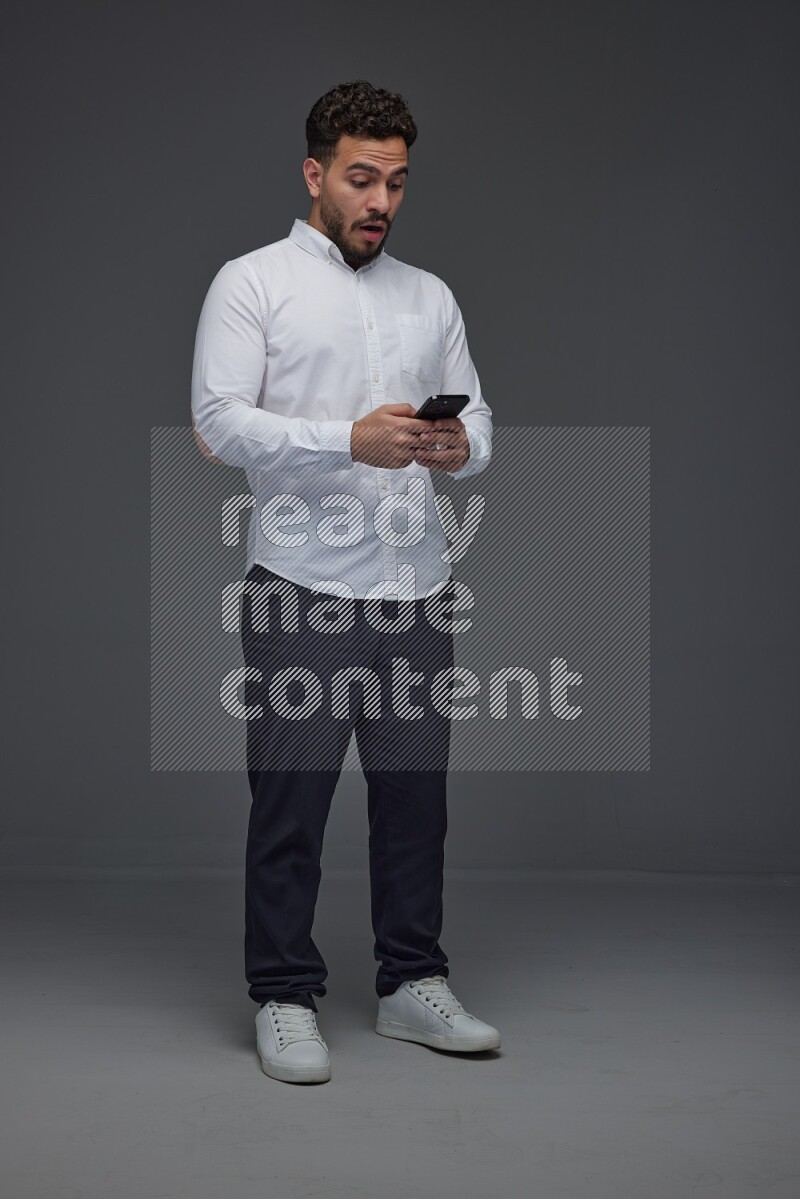 A man wearing smart casual standing and using his phone eye level on a gray background