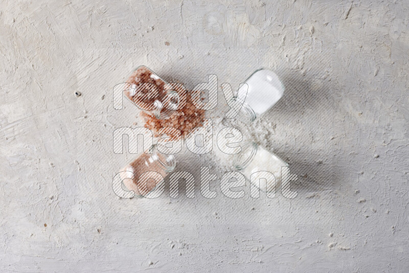 4 glass jars filled with table salt, coarse sea salt, fine himalayan salt and coarse himalayan salt on white background