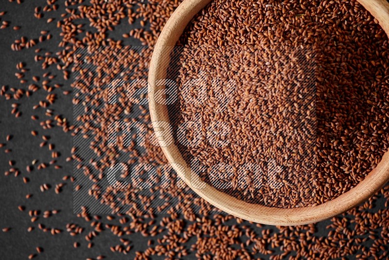 A wooden bowl full of garden cress surrounded by seeds on a black flooring in different angles