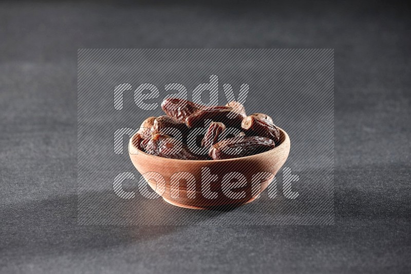 A wooden bowl full of dried dates on a black background in different angles