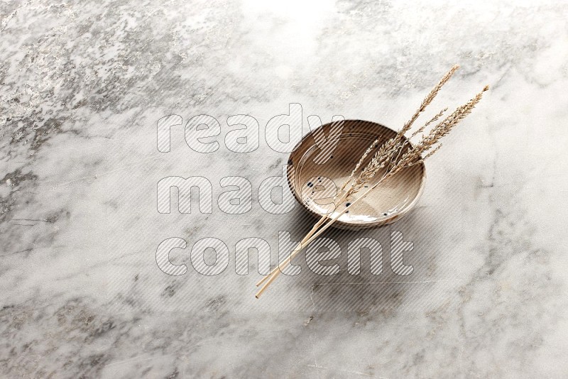 Wheat stalks on Multicolored Pottery Bowl on grey marble flooring, 45 degree angle