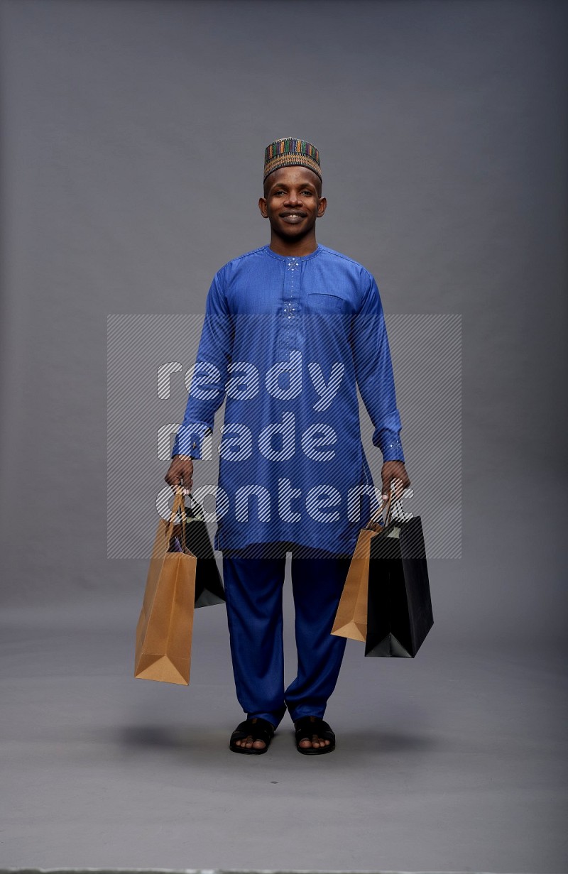 Man wearing Nigerian outfit standing holding shopping bag on gray background