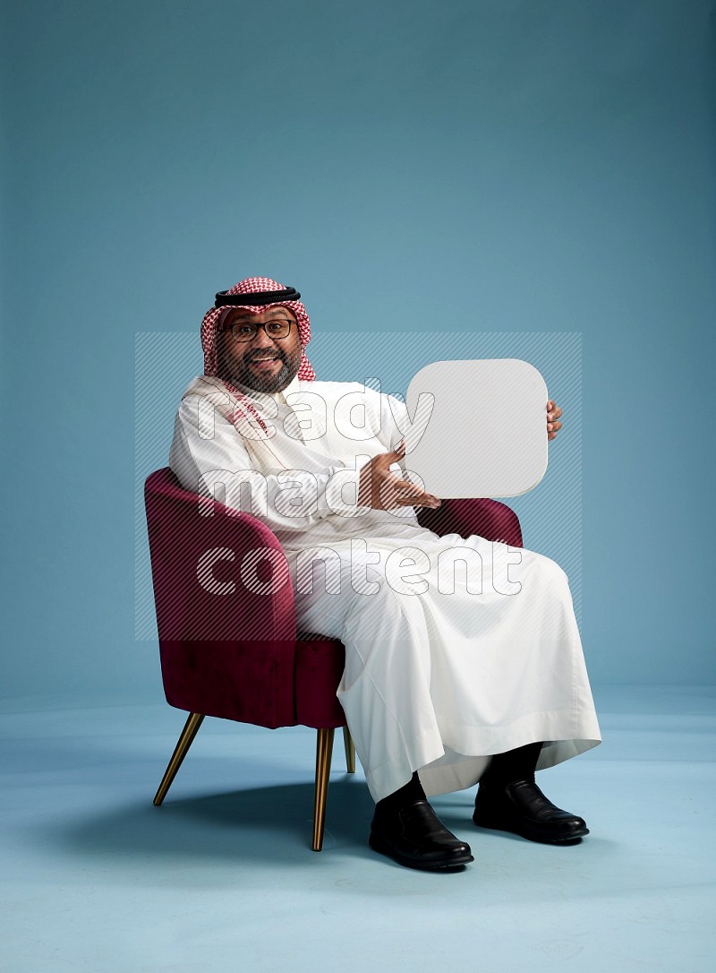 Saudi Man with shimag sitting on chair holding social media sign on blue background