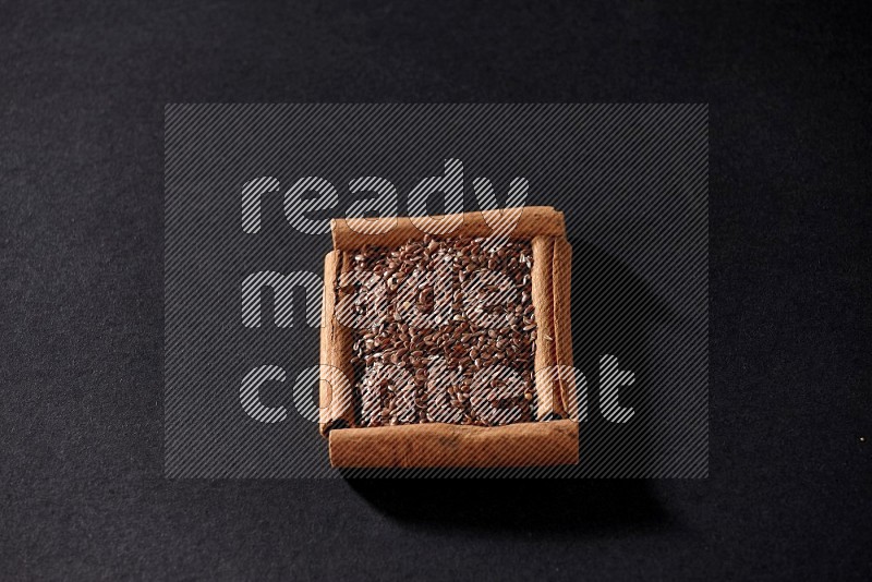 A single square of cinnamon sticks full of flaxseeds on black flooring