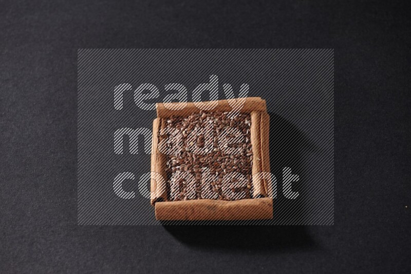 A single square of cinnamon sticks full of flaxseeds on black flooring