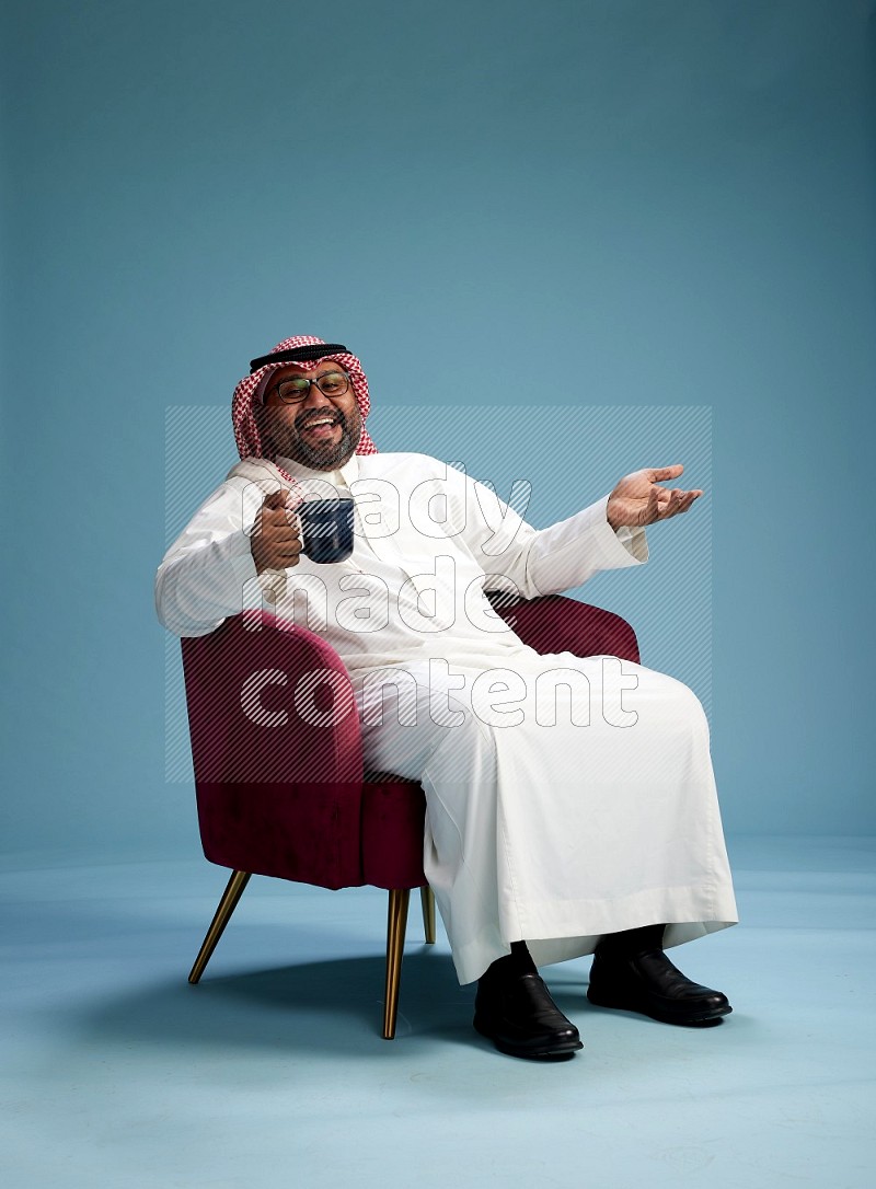 Saudi Man with shimag sitting on chair drinking coffee on blue background