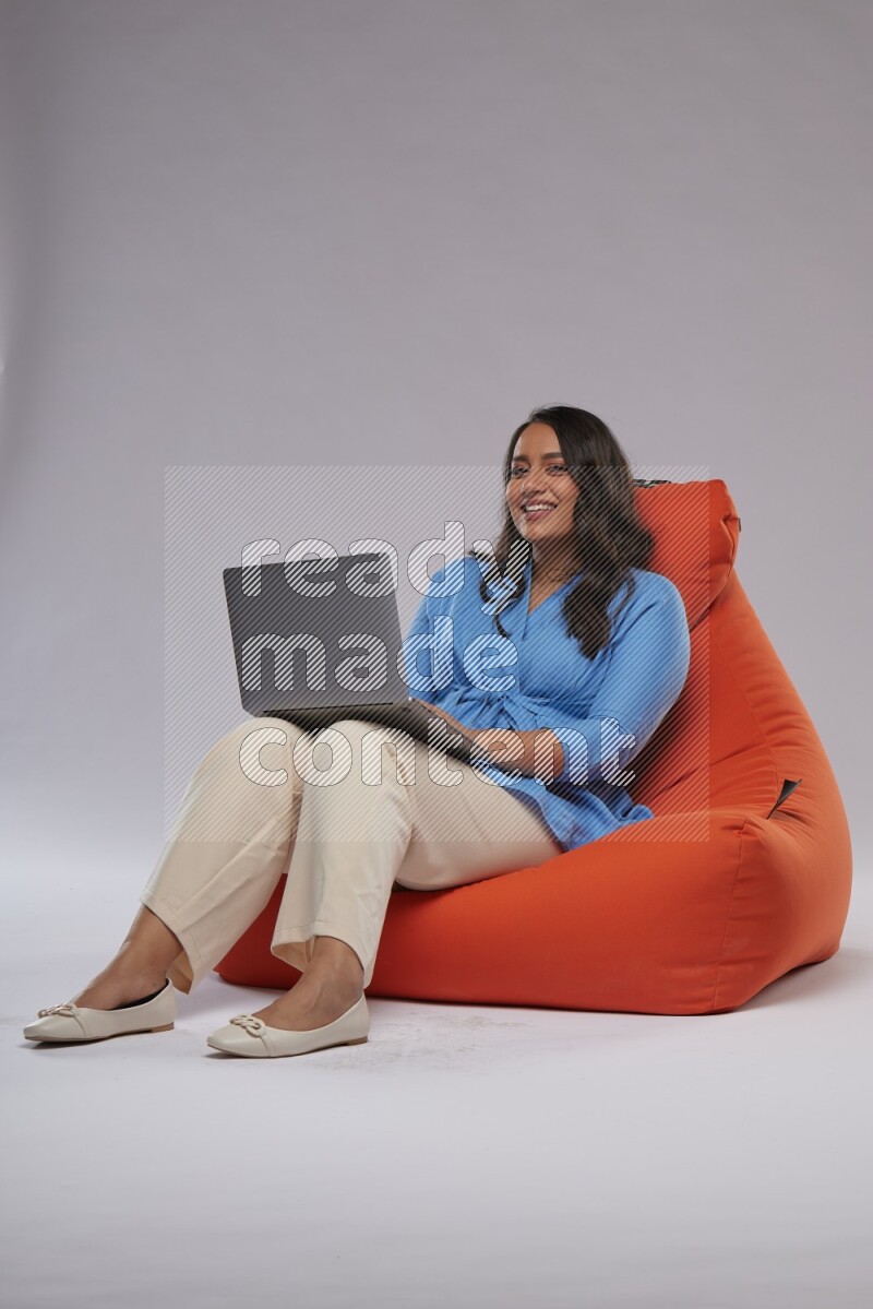 A woman sitting on an orange beanbag and working on laptop