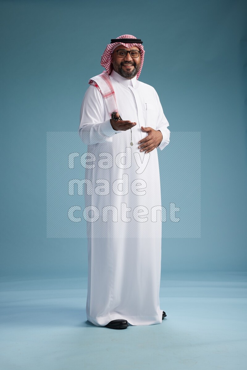 Saudi Man with shimag Standing Interacting with the camera on blue background
