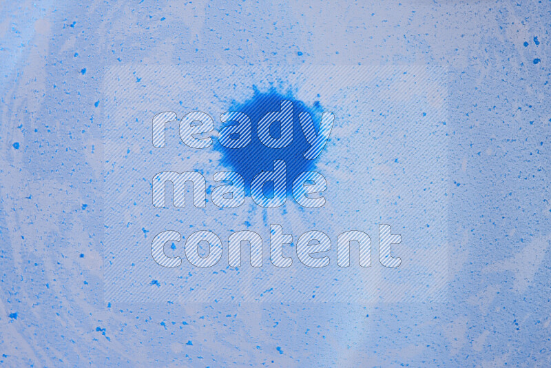 The image captures a dramatic splatter of blue paint over a blue backdrop