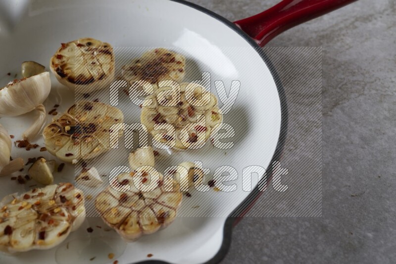 half's roasted garlic in a red-coated cast iron pan on a grey textured countertop