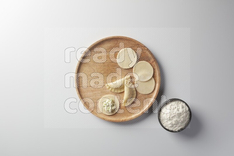 two closed sambosas and one open sambosa filled with cheese while flour aside in a wooden dish on a white background