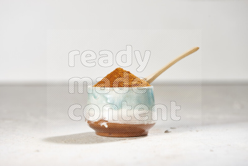 A colored pottery bowl full of ground paprika powder on white background