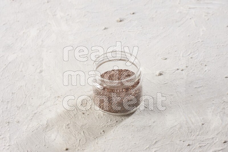 A glass jar full of flax seeds on a textured white flooring