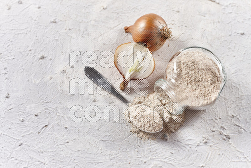 A glass jar full of onion powder flipped with some spilling powder on white background