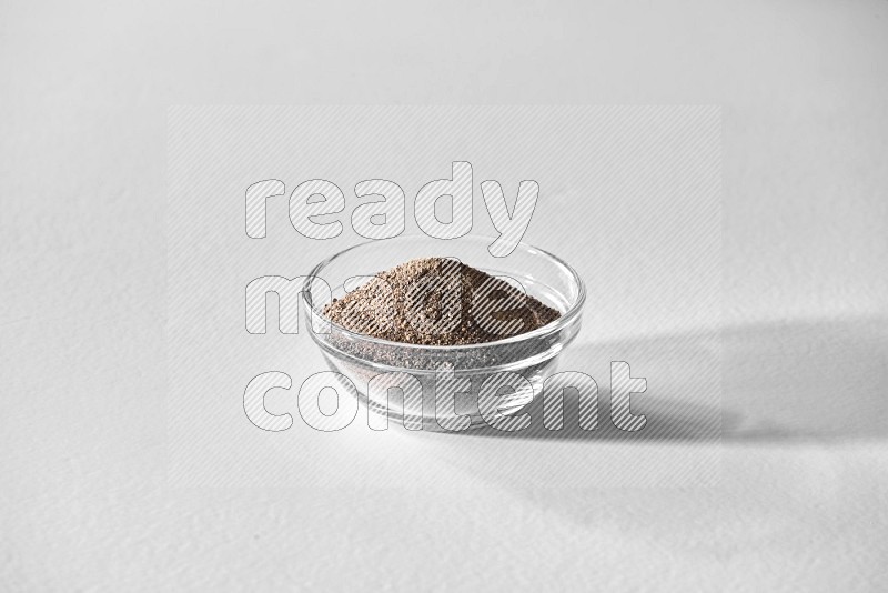 A glass bowl full of black pepper powder on white flooring