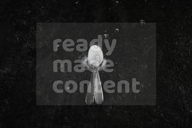 ملعقتان معدنيتان ممتلئتان بالملح الأبيض على خلفية سوداء